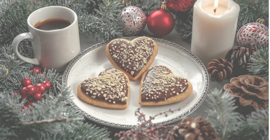 Lebkuchenkekse in Herzform auf einem Teller, umgeben von Kerzen und winterlicher Dekoration